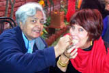 Indra Rai feeds Barbara Adams Indian appetizers so that the henna designs on her hands can dry.